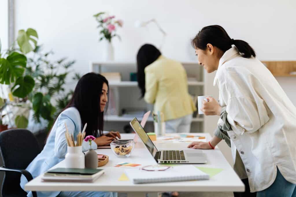 Employee sitting at desk asking coworker leaning over desk for feedback