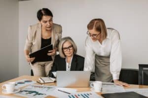 three women working in commercial banking huddled over desk looking at laptop